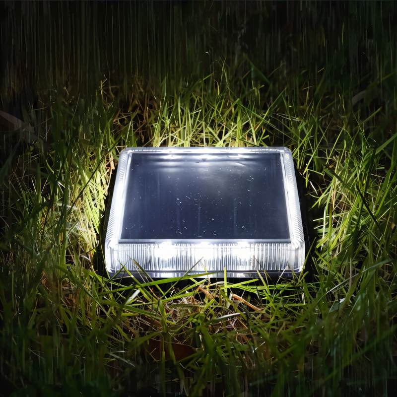 Clérachic square solar light shining cool white from its ribbed lens, sitting in wet grass at night.