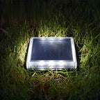 Clérachic square solar light shining cool white from its ribbed lens, sitting in wet grass at night.