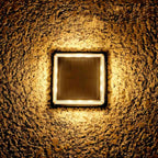 Top-down view of a Clérachic square solar light glowing warm, set into rough stone with a dark panel at its centre.