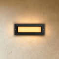 Clérachic small rectangular outdoor step light in dark grey with a frosted panel glowing warm white on a plaster wall.