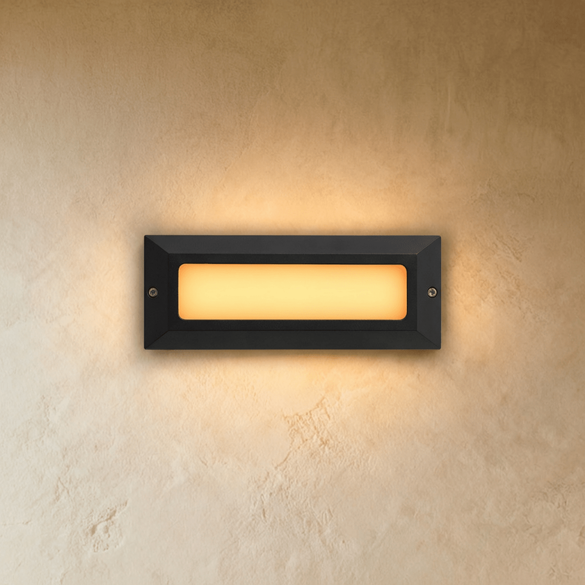 Clérachic small rectangular outdoor step light in dark grey with a frosted panel glowing warm white on a plaster wall.