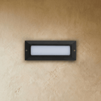 Clérachic small rectangular step light in dark grey with the frosted diffuser unlit, two fixing screws on a plaster wall.