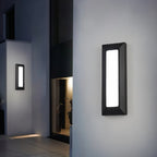 Clérachic dark grey vertical wall light with a bright white panel on a pale rendered wall at an entrance after dark.