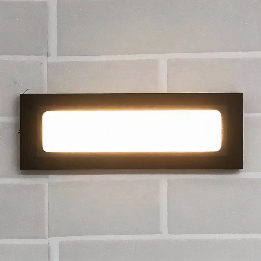 Close view of a Clérachic dark rectangular wall light with a bright warm glowing panel mounted on pale grey brick.