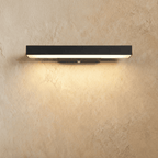Clérachic long black aluminium bar wall light with a warm white glow washing down a textured limewashed wall, small sensor on the bracket.