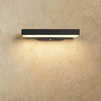 Clérachic mid-length black aluminium bar wall light lit warm white, with a slim wall bracket and sensor, on a limewashed wall.