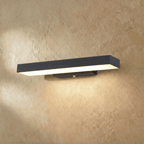 Clérachic black aluminium bar wall light seen at an angle, glowing warm white, with its opal diffuser and slim wall plate.