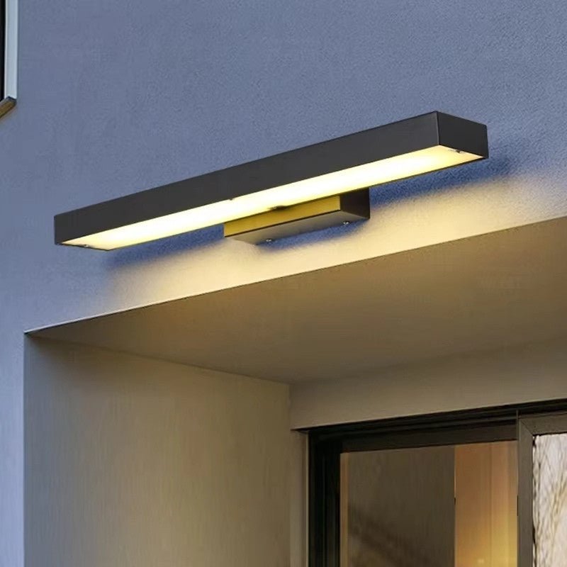 Clérachic black bar wall light fixed to an exterior wall above a doorway under a canopy, casting a warm glow over the render.