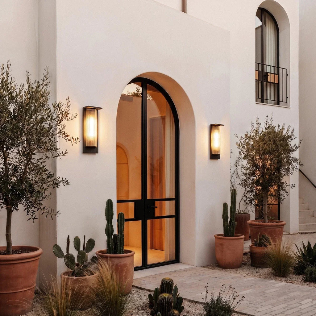 Pair of Clérachic black outdoor wall lights with ribbed shades flanking an arched glass door, among terracotta pots and cacti