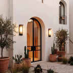 Pair of Clérachic black outdoor wall lights with ribbed shades flanking an arched glass door, among terracotta pots and cacti