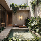 Clérachic black outdoor wall light with a ribbed shade on a concrete courtyard wall above a daybed, plunge pool and tropical plants