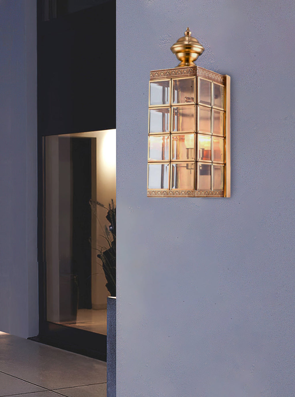 Lit Clérachic brass and glass wall light on a mauve-grey wall beside a dark doorway, the lantern high above the entrance.