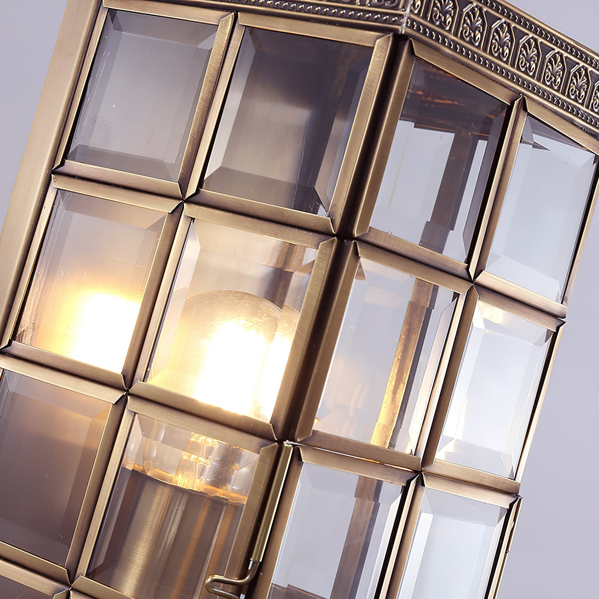 Close view of the bevelled glass panes and brass framing on this Clérachic wall light, with the lit bulb glowing inside.