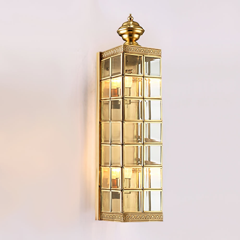 Longer Clérachic brass and glass wall light, lit, on a soft pink-white wall, with seven rows of glass panes up its body.