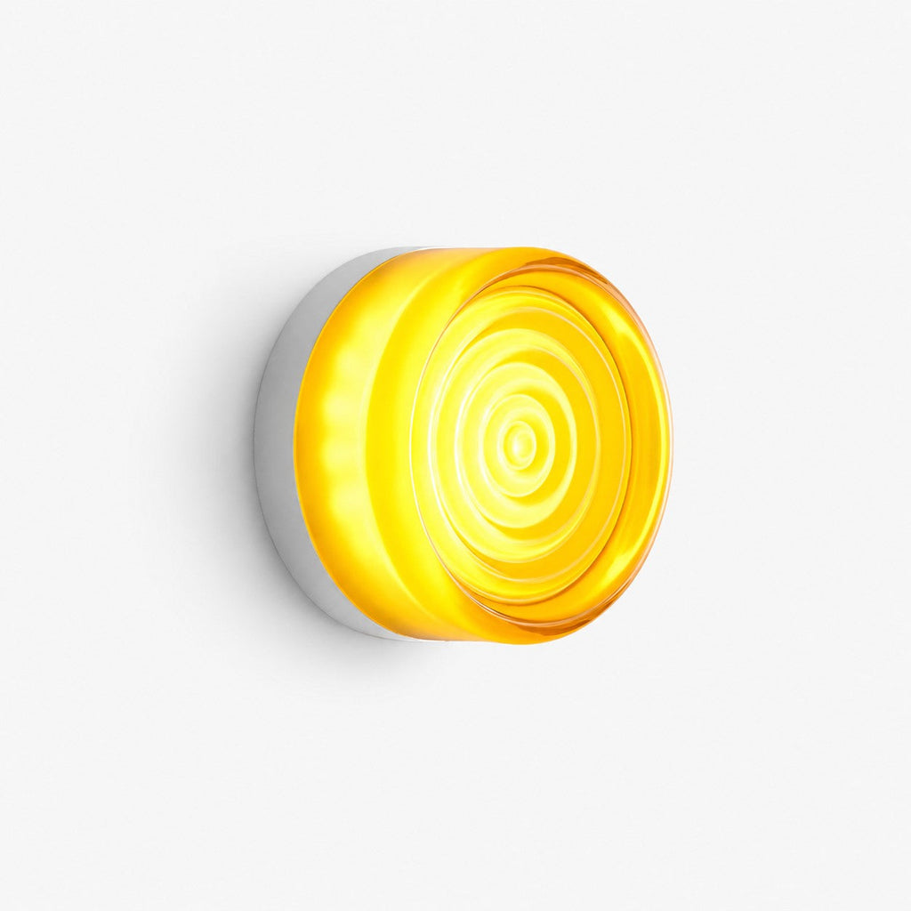 Round glass wall light with rippled concentric rings glowing yellow, on a plain white backdrop, from Clérachic.
