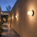 Row of white-glass Clérachic wall lights receding down a long rendered passage wall, the nearest shown large in the foreground.