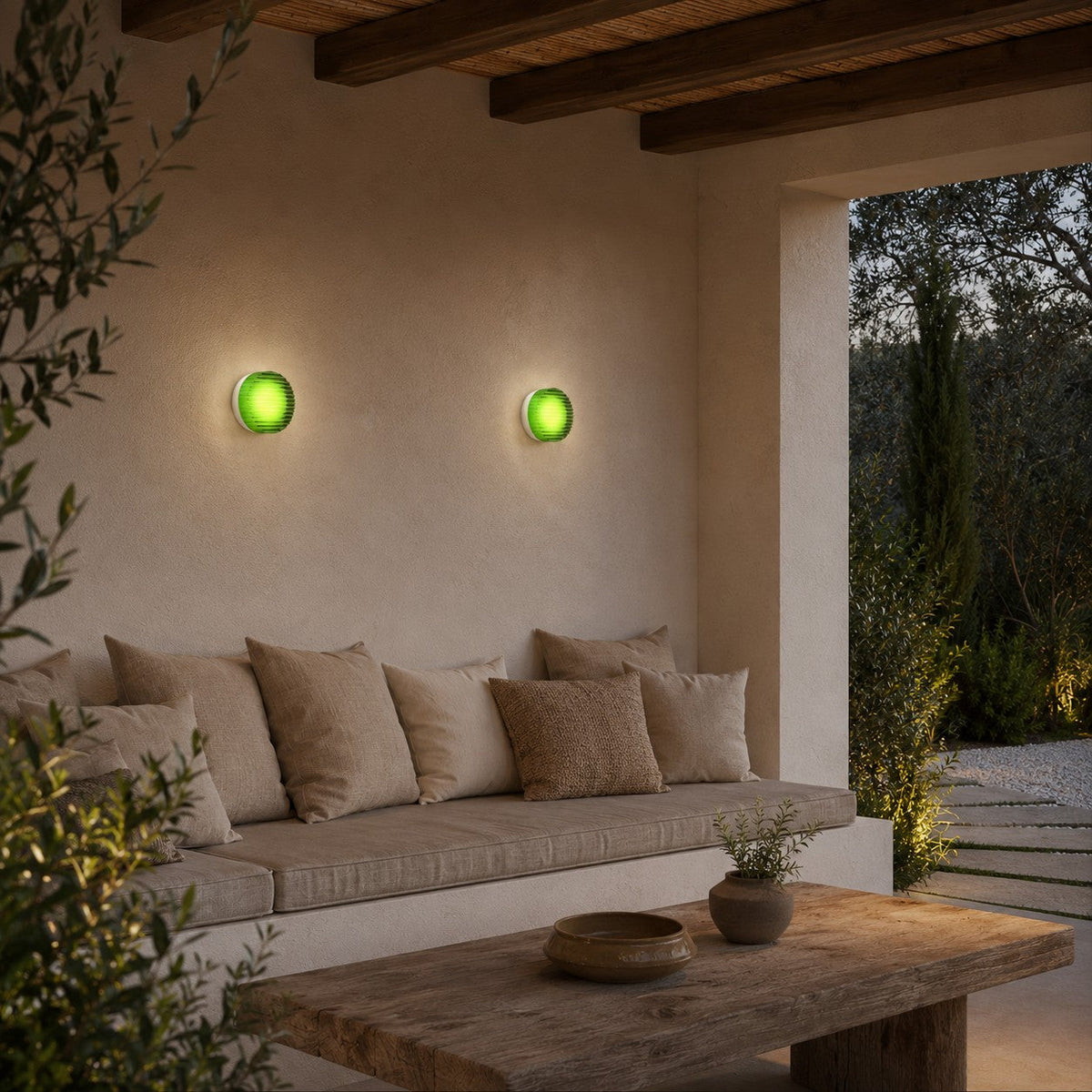 Two green-glass Clérachic wall lights above an outdoor sofa under a timber-beamed terrace, with a rustic coffee table below.
