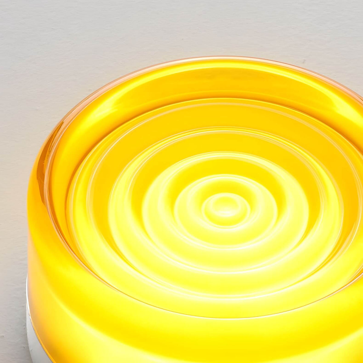 Close view of the rippled concentric glass face of this Clérachic wall light, glowing in a vivid yellow.