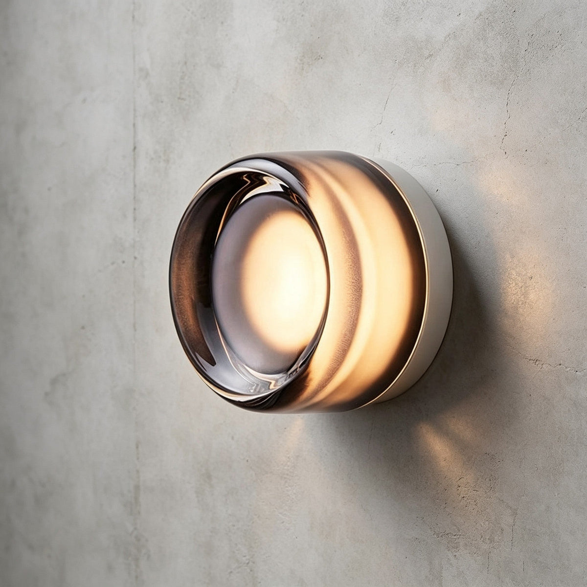 Smoke grey glass version of this Clérachic wall light, its clear lens lit warm at the centre, on a concrete wall.