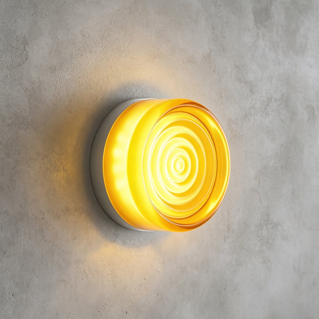 Yellow glass Clérachic wall light with concentric ripples on its face, lit and mounted on a grey concrete wall.