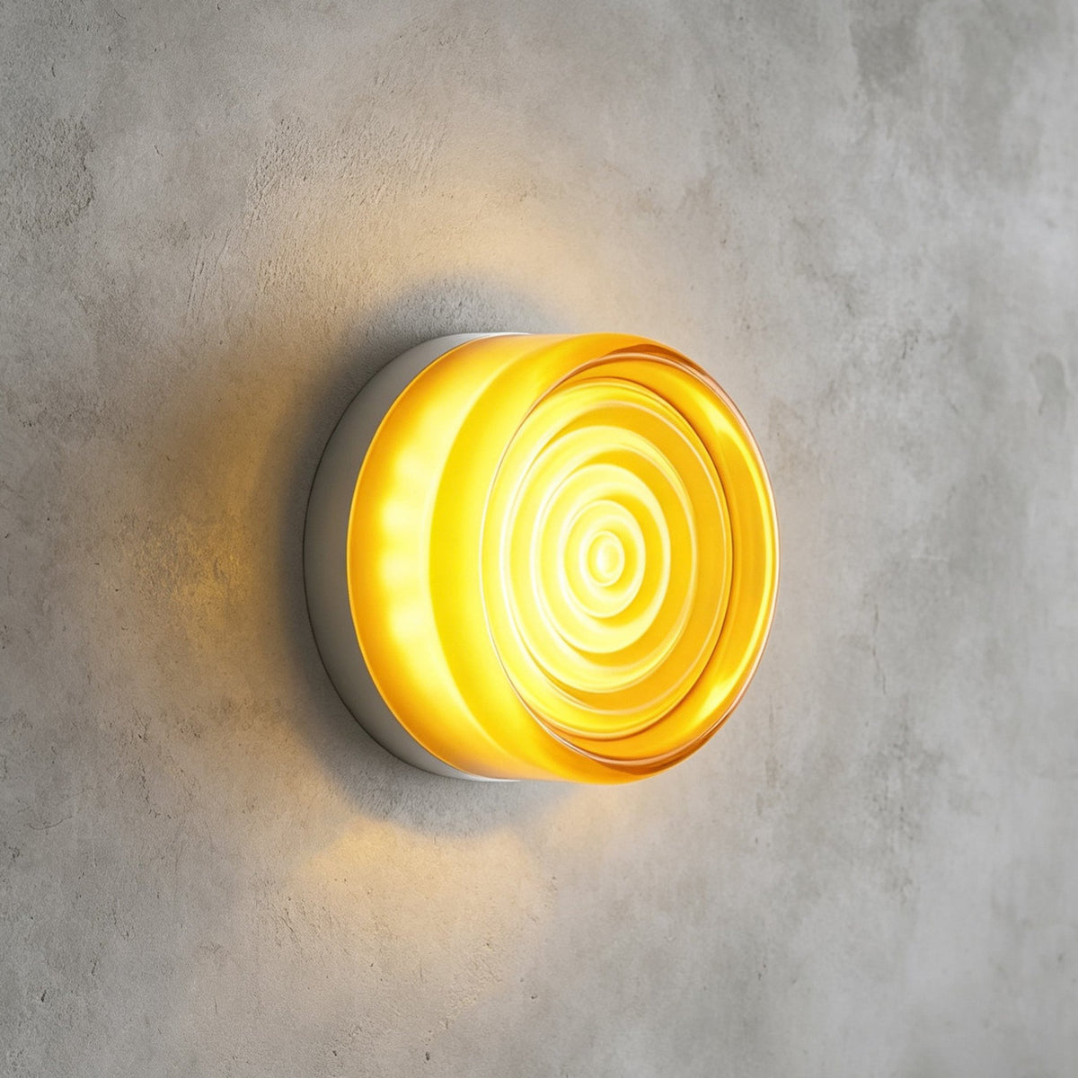 Yellow glass Clérachic wall light with concentric ripples on its face, lit and mounted on a grey concrete wall.