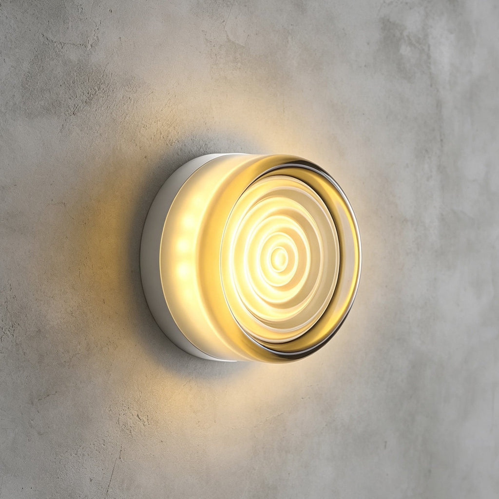 Clear rippled-glass Clérachic wall light with a pale tint at the rim, glowing warm on a grey concrete wall.