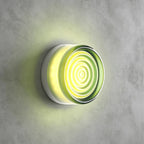 Pale green rippled-glass Clérachic wall light glowing lime against a grey concrete wall, a faint green halo around it.