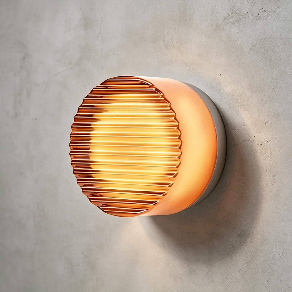 Amber ribbed-glass Clérachic wall light with a copper-toned glow, mounted on a rough grey concrete wall.