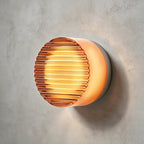 Amber ribbed-glass Clérachic wall light with a copper-toned glow, mounted on a rough grey concrete wall.
