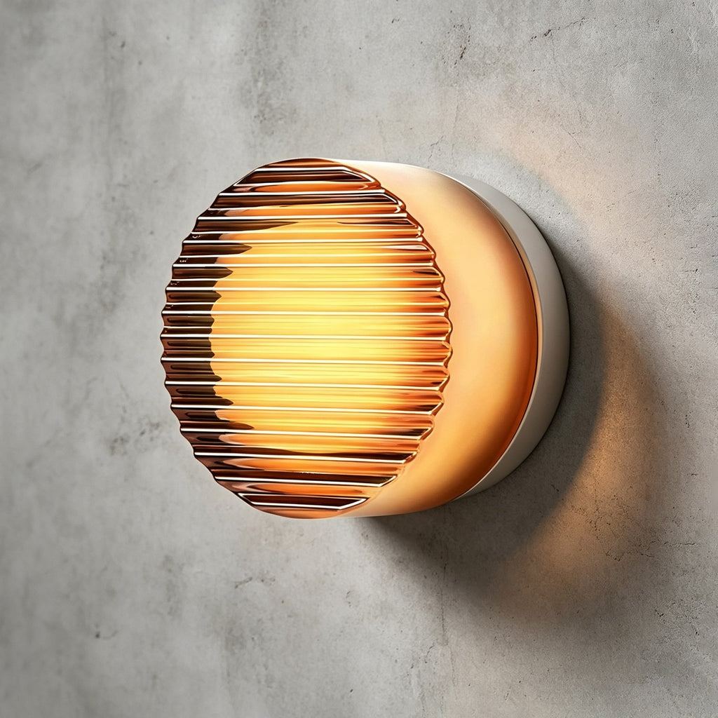 Ribbed-face Clérachic wall light in amber glass with a bright core, seen at an angle on a grey concrete wall.