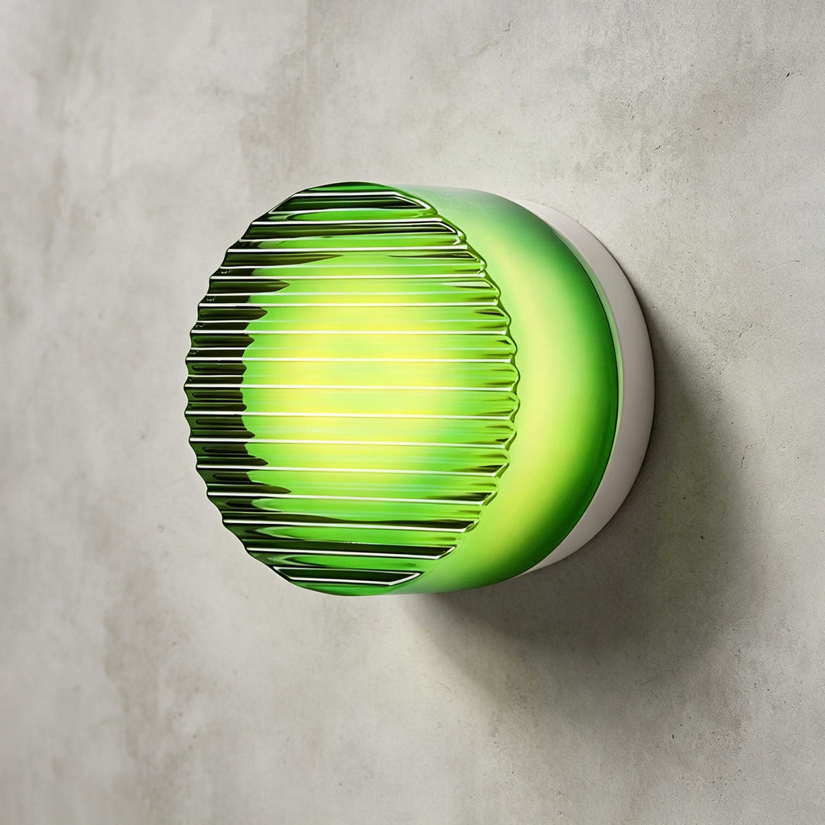 Green ribbed-glass Clérachic wall light glowing bright green behind its ridged clear face, on a concrete wall.