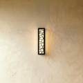 Clérachic tall narrow black wall lamp with a cut-out geometric pattern, glowing warm white against a pale limewash wall.