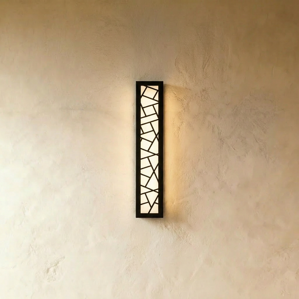 Clérachic taller black wall lamp with a fractured geometric cut-out grille, its opal diffuser glowing on a warm plaster wall.