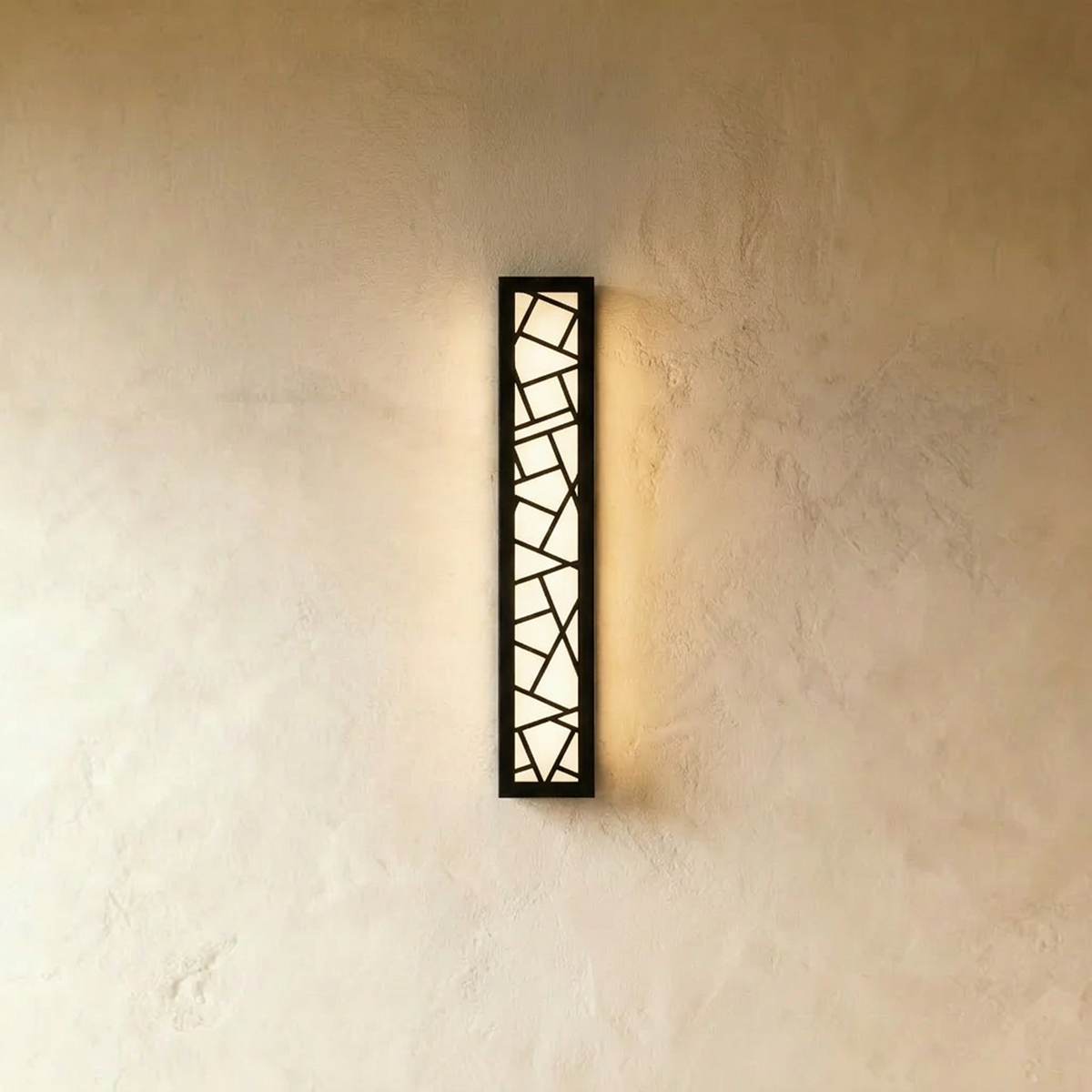 Clérachic extra-long black wall lamp with an angular cut-out pattern and a warm white glow, hung on a limewash plaster wall.
