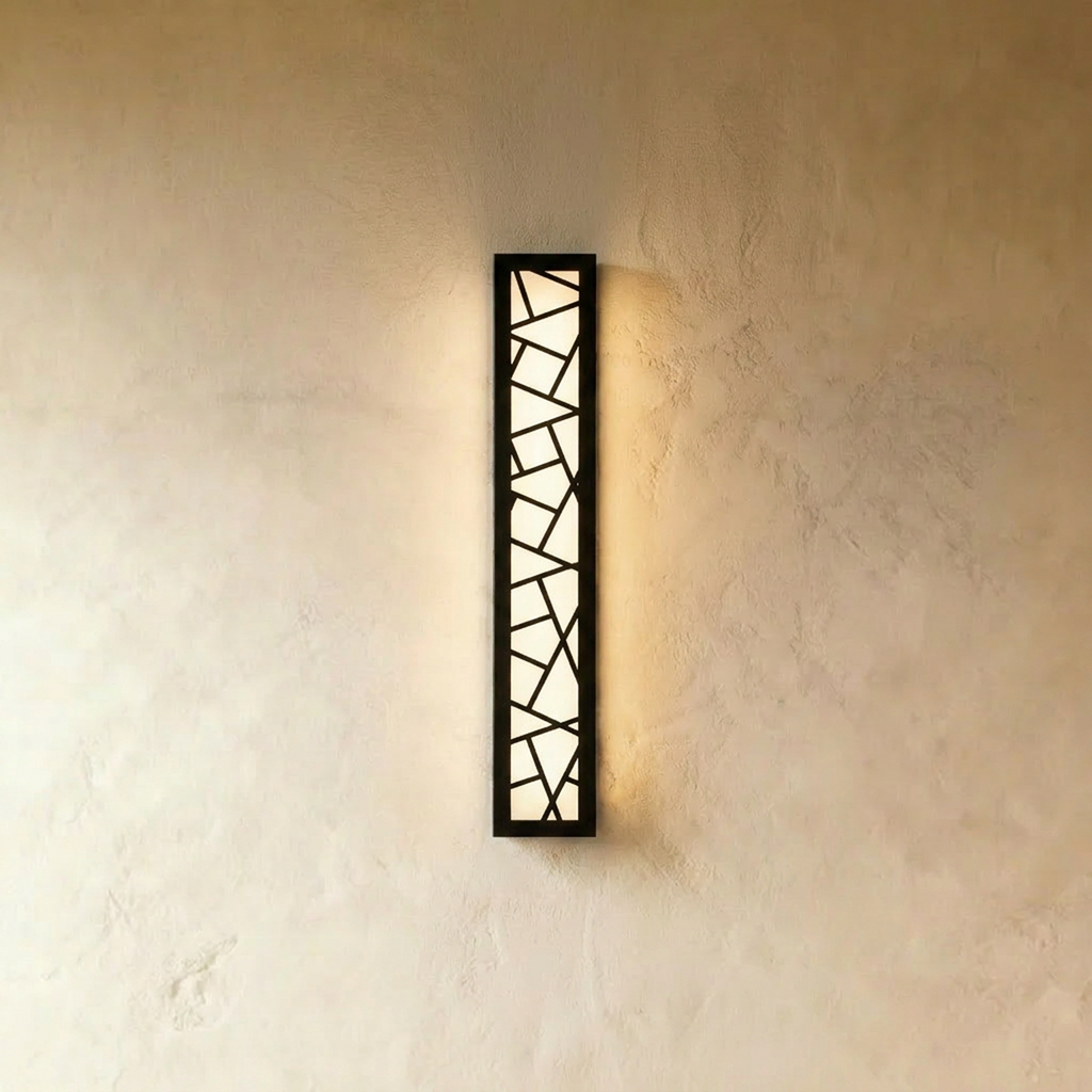 Clérachic long vertical black wall lamp with a geometric cut-out grille, lit evenly in warm white on a plaster wall.