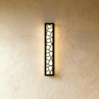 Clérachic long vertical black wall lamp with a geometric cut-out grille, lit evenly in warm white on a plaster wall.
