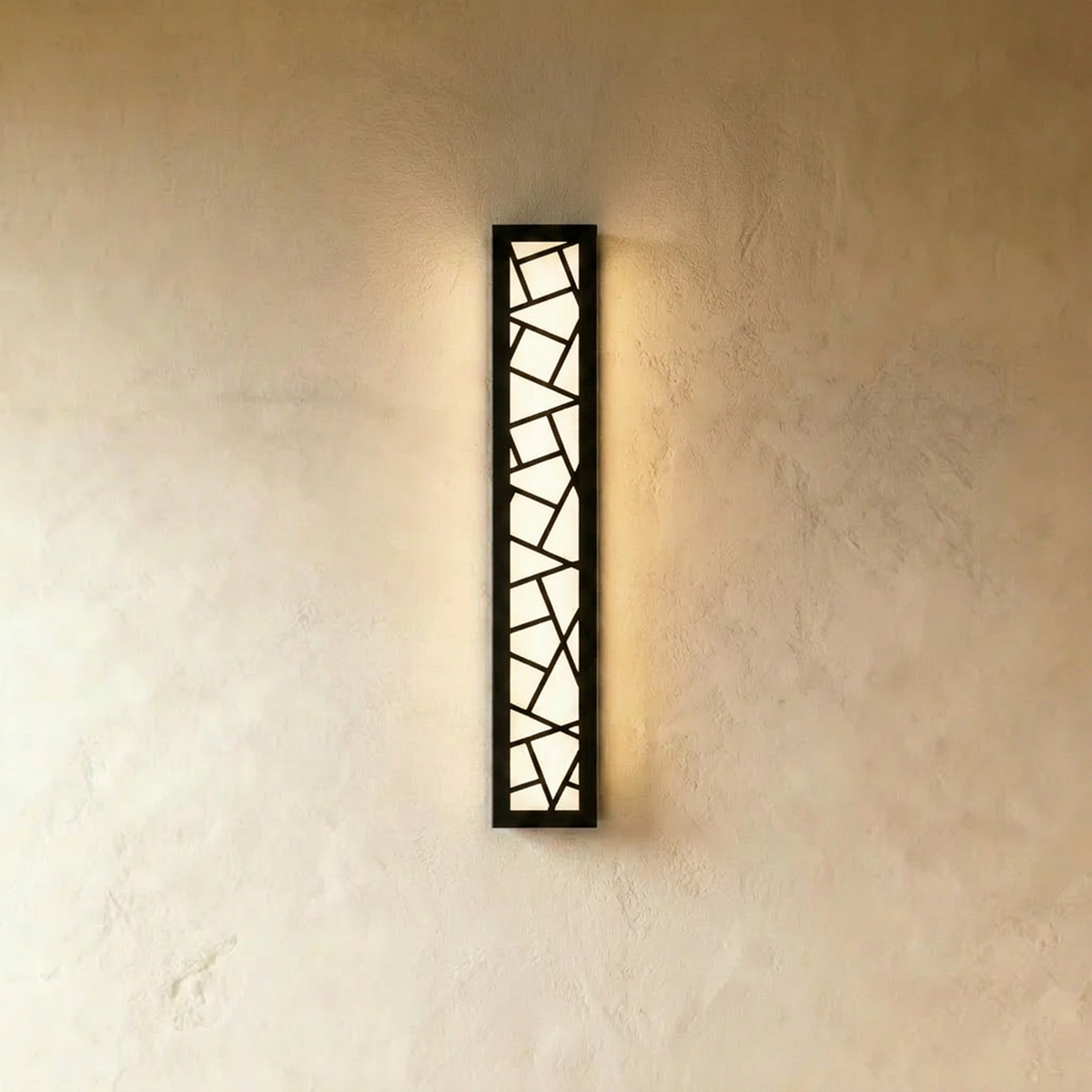 Clérachic tall slim black wall lamp with an angular cut-out front, glowing softly against a warm textured plaster wall.
