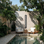 Clérachic tall black cut-out wall lamp on a concrete garden wall above two cream armchairs, beside a plunge pool.