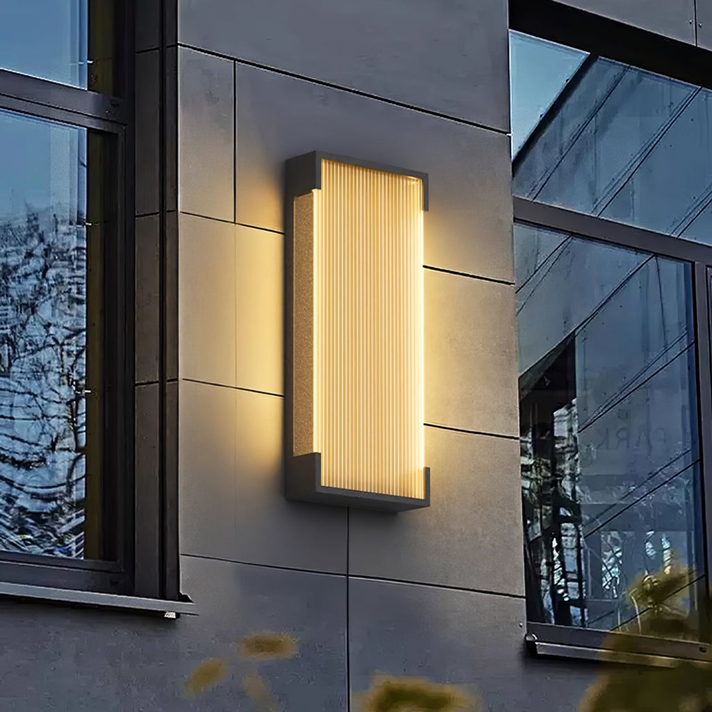 Lit rectangular wall light from Clérachic on a grey cladded wall beside a window, casting a warm glow around it.