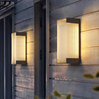 A pair of deeper Clérachic wall lights on grey timber cladding, their ribbed panels lit warm from within.