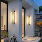 Two Clérachic ribbed wall lights flanking a glazed front door on a white entrance, with a plant and a side table.