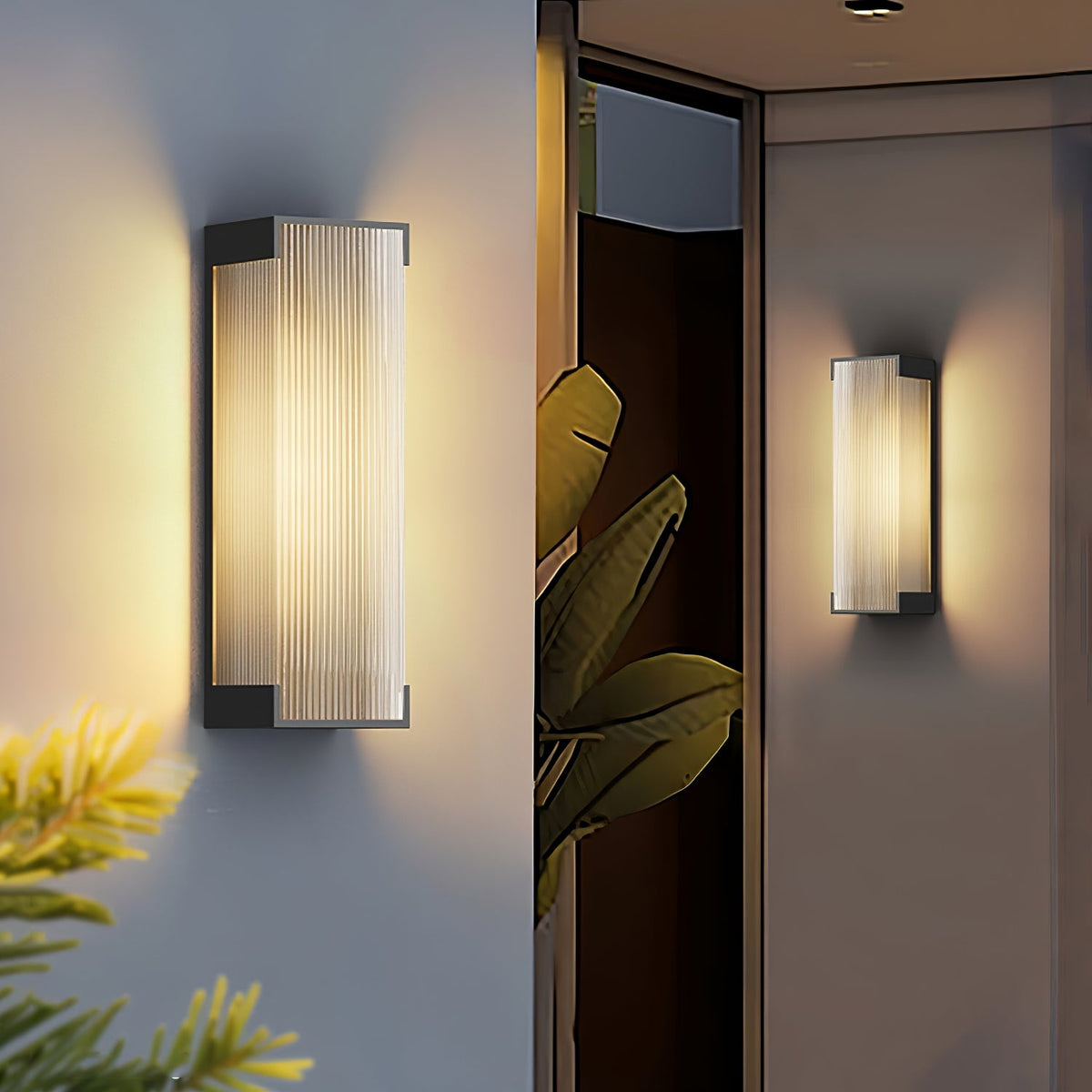 Close-up of a Clérachic ribbed wall light glowing warm on a pale wall, with palm leaves and a second light behind.