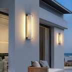 Clérachic wall lights on a white modern house at dusk, with a wicker sofa on the terrace and the sea beyond.