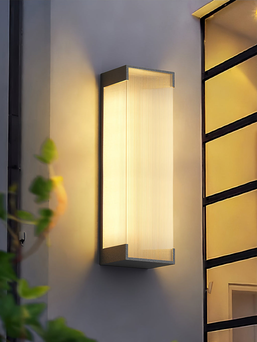 Tall Clérachic ribbed wall light glowing against a pale rendered wall, with a dark-framed glazed door at its side.