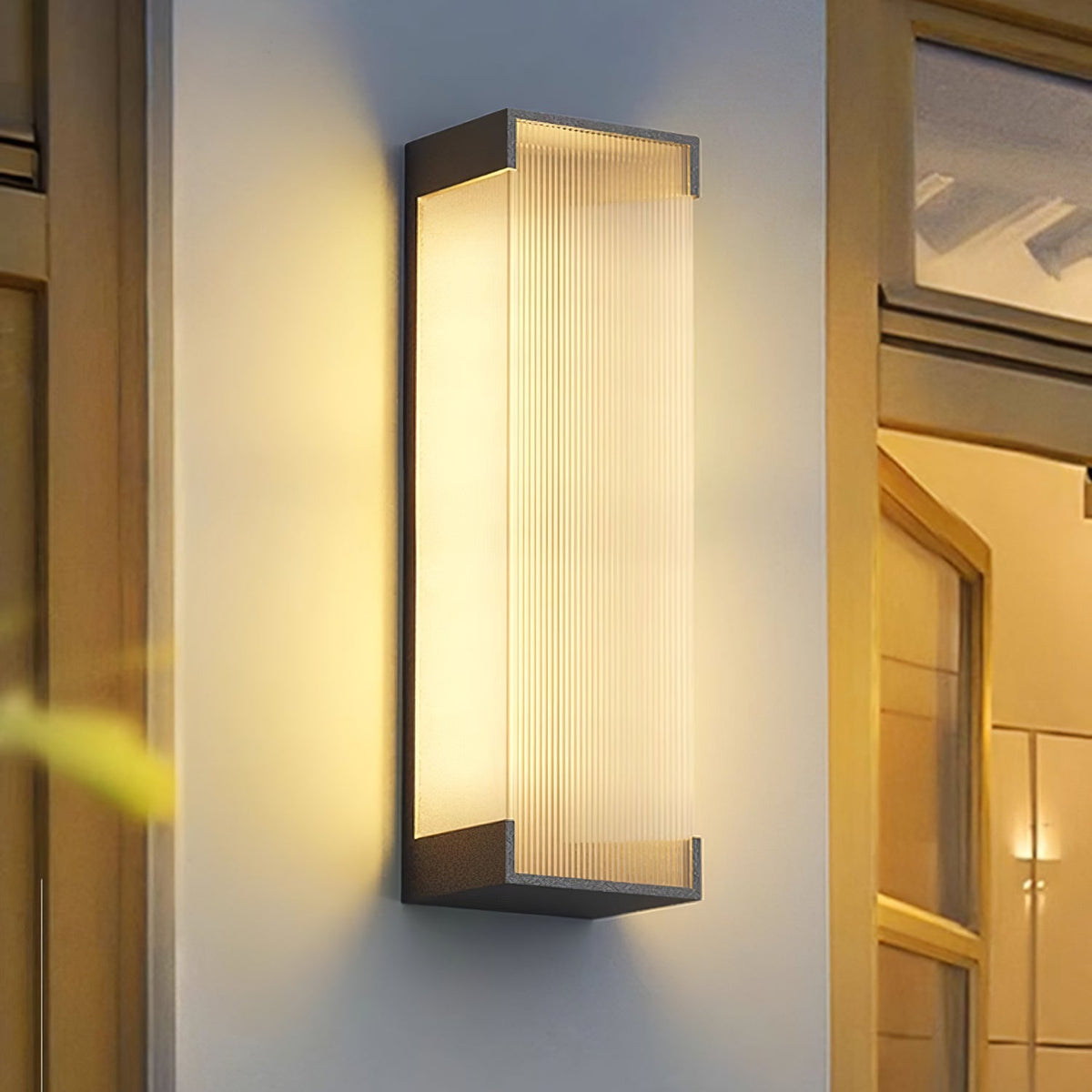 Close view of a tall Clérachic wall light, its ribbed panel lit warm, on a white wall beside a timber door frame.