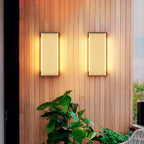 Pair of upright Clérachic wall lights on a warm timber-clad wall, with green foliage in front of them.