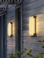 Two Clérachic wall lights, one smaller and one larger, lit warm on grey cladding either side of a doorway.