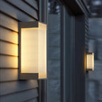 Close view of a deeper Clérachic wall light on grey clapboard, its ribbed panel lit warm, with a second light beyond.
