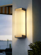 Clérachic wall light lit on a roughcast pale wall, with a striped awning and a view of the water to one side.