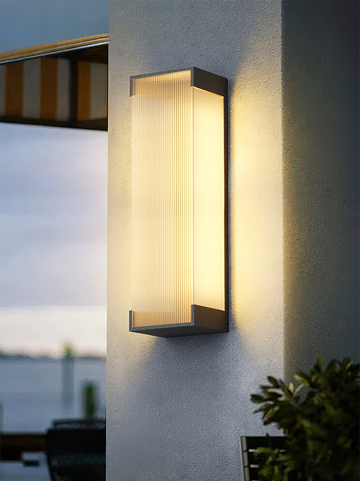 Clérachic wall light lit on a roughcast pale wall, with a striped awning and a view of the water to one side.